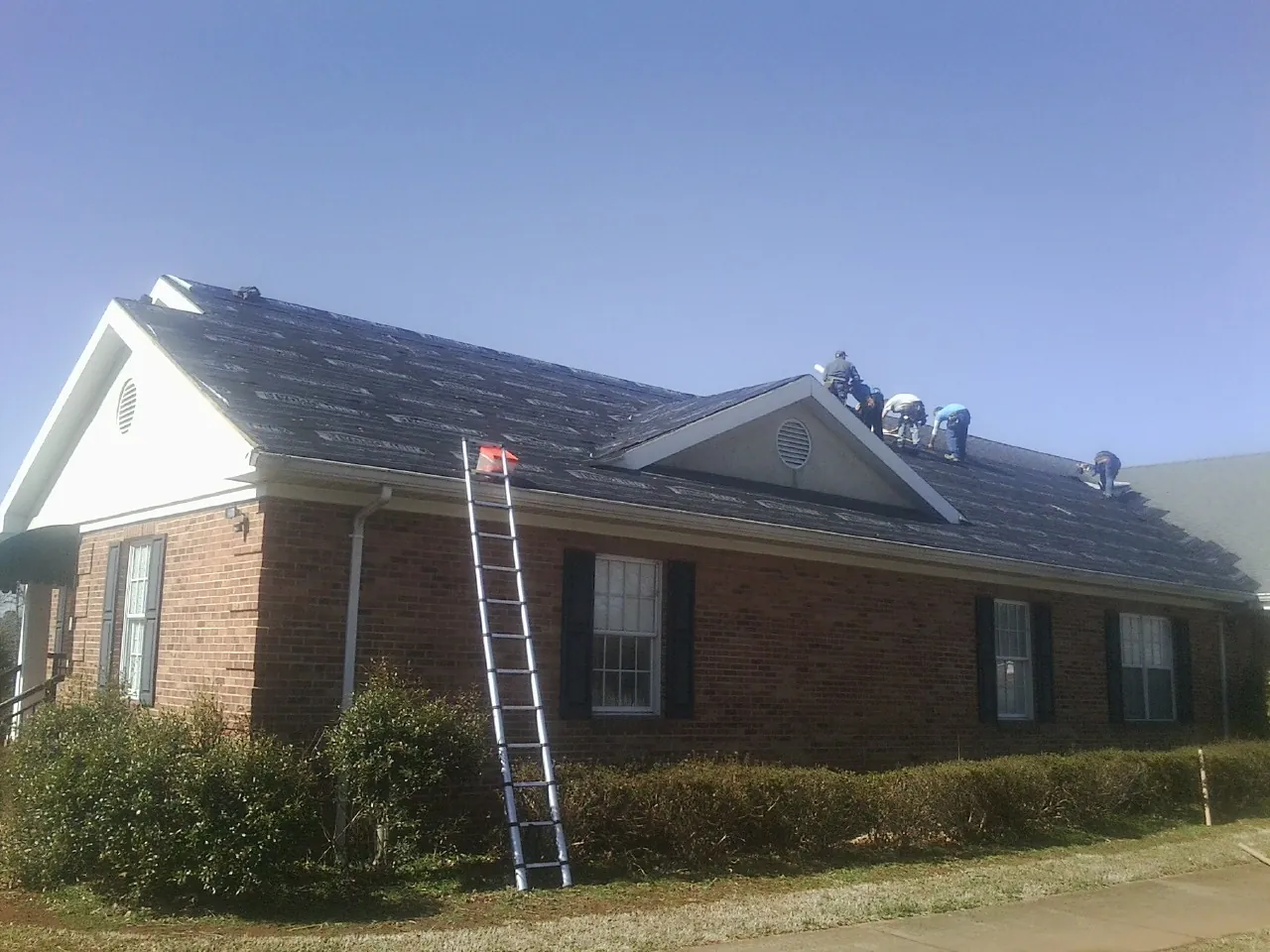 Crew tearing shingles off a brick ranch roof with a ladder set — Emergency Roof Repair work by our crew in Kodak
