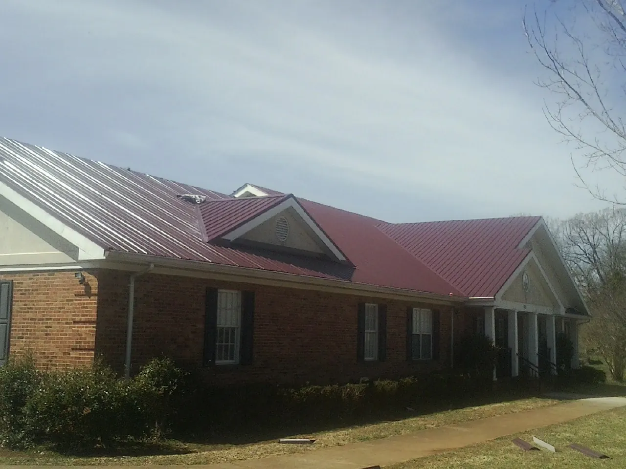 Red metal roof with gabled entries on a long brick building, from a Hail Damage Roof Repair job in Kodak