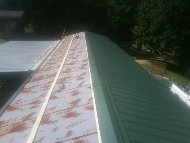 Old rusted panels beside newly installed green metal roofing — Wind Damage Roof Repair by Roofing Brothers in Kodak