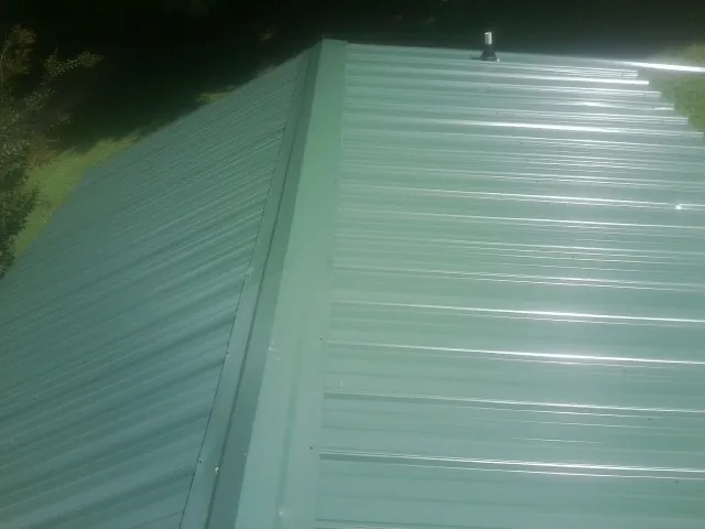 New green metal panels meeting at the ridge of a roof — Flat Roof Repair work by our crew in Kodak