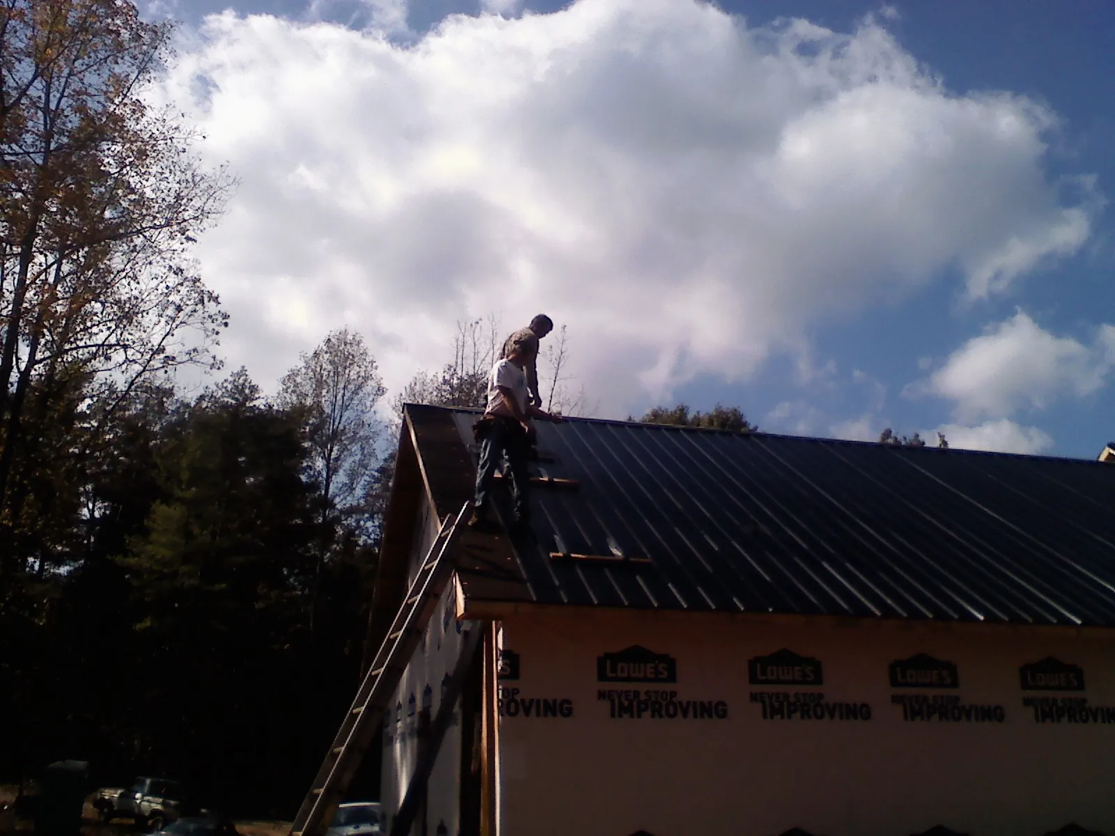 Roofer fastening dark metal panels high against a cloudy sky, from a Roof Inspection job in Kodak