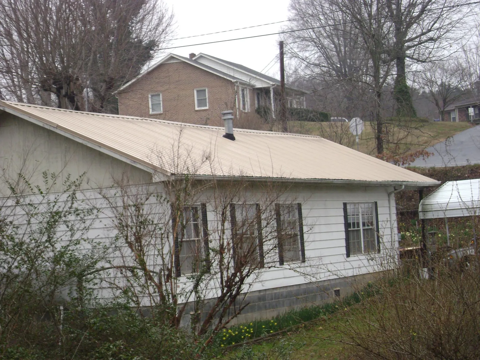 Tan metal roof on a white sided house set into a hillside — Commercial Roofing by Roofing Brothers in Kodak