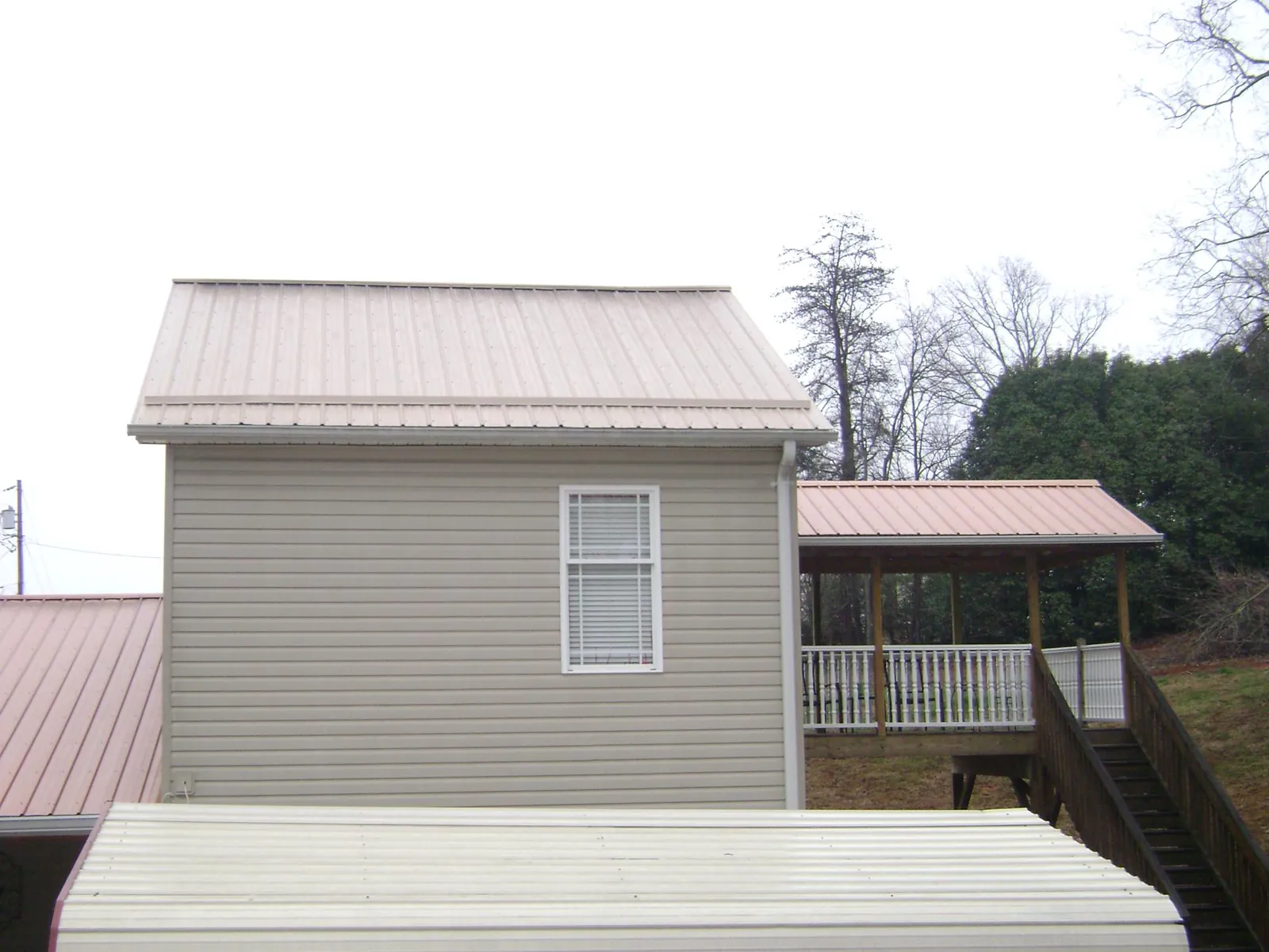 Tan metal roofs on a two story addition and attached porch, from a Roof Replacement job in Kodak